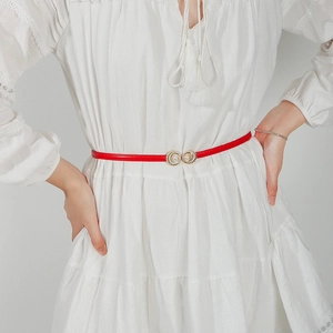 Detail of red slim belt with gold pearl buckle on a white dress for women