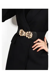 Detail of elastic waist belt featuring a gold floral buckle with white pearl accents