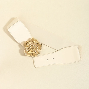 Detail shot of a large golden metal flower buckle on a cream elastic waist belt for women