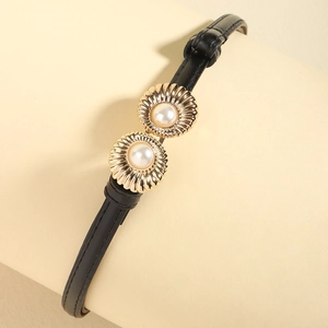 Detail of elegant gold flower buckle with pearls on a slim black leather belt for women