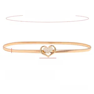 Detailed view of a slim gold elastic waist belt with a sparkling rhinestone heart buckle