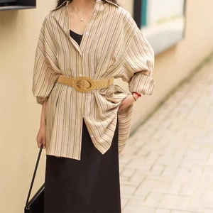 Detail of a woven straw waist belt with an oval buckle on a khaki striped shirt
