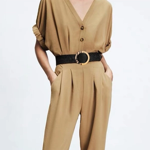 Detail of a thin black woven belt with a round wood-style buckle on a khaki jumpsuit