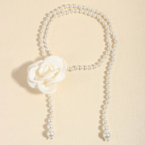 Detail of elegant pearl waist chain featuring a white camellia flower on a textured surface