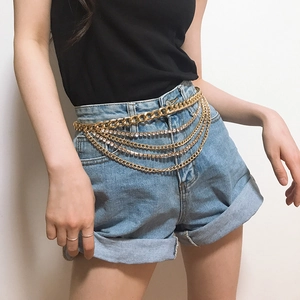 Detail of multilayer gold waist chain featuring crystals and Cuban link chains on a model