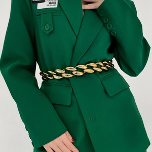 Close-up of a chunky gold acrylic chain belt paired with a dark green blazer jacket