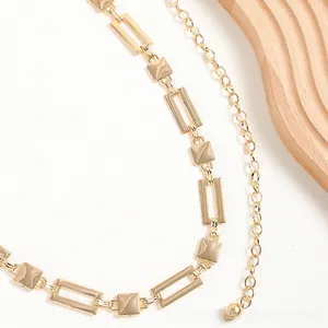 Detail of gold geometric link waist chain with rectangular and square hollow metal patterns