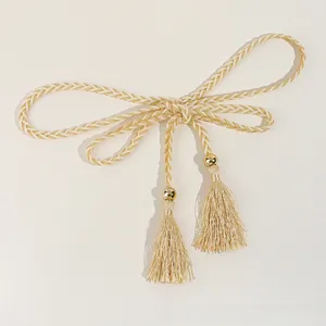 Close-up of woven waist rope with gold beads and fringe tassels on a textured surface