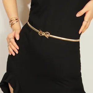 Detail of a thin gold metal waist chain with a bow buckle on a black dress