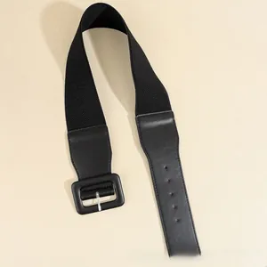 Detail of black wide elastic waist belt with faux leather texture and metallic square buckle