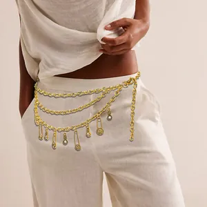 Detail of bohemian gold multi-layer waist chain with pin and coin pendants on white pants
