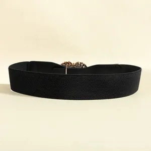 Detail of black elastic wide belt featuring a gold hollow floral decorative buckle