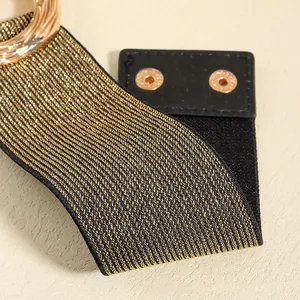 Detail of elegant black elastic waist belt with gold metallic thread and circular buckle