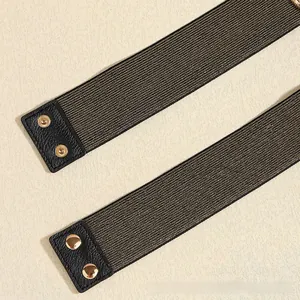 Detail of black elastic belt with textured leather ends and gold metal snap buttons
