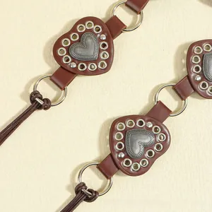Detail of dark brown leather heart belt with metal eyelets and vintage metal heart buckle