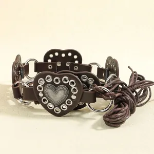Close-up of brown leather punk belt featuring vintage metal heart buckles and woven cord