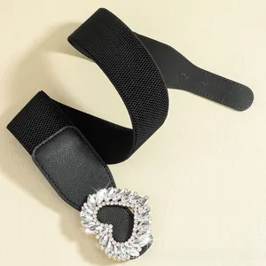 Detail of a wide elastic belt featuring a sparkling rhinestone heart buckle on black leather