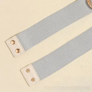 Detail of silver elastic waist belt featuring cream leather ends and gold metal buttons