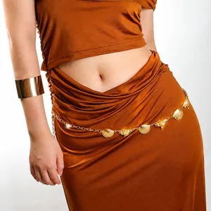 Detail of bohemian gold shell chain belt and sleek metallic cuff bracelet on a model
