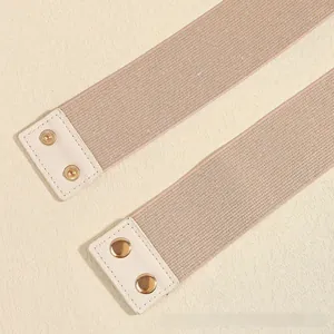 Detailed view of beige elastic wide waist belts with white faux leather snap fasteners