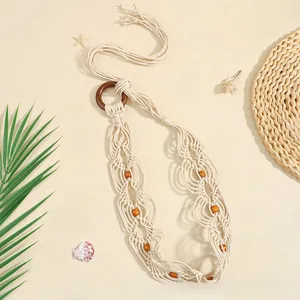 Détail d'une ceinture en macramé bohème avec perles en bois et anneau sur fond de sable