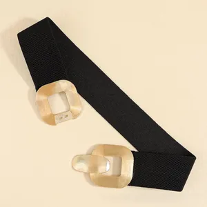 Detail of interlocking gold geometric metal buckles on a black elastic wide waist belt