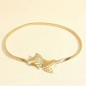 Detail of a bright gold elastic belt featuring a textured leaf-shaped metal buckle design