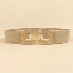 Detailed view of wide elastic beige waist belt with large geometric golden buckle