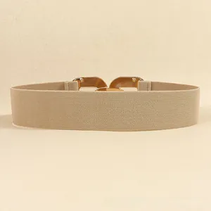 Close-up of beige elastic waist belt with modern gold geometric interlocking metal buckle