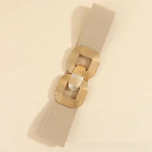 Close-up of golden geometric double ring buckle with brushed texture on beige elastic belt