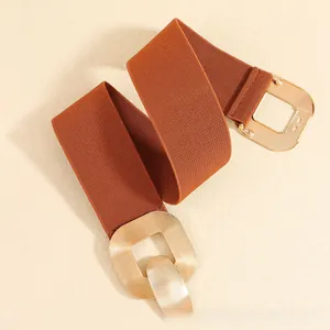 Detail of caramel brown elastic wide belt featuring a large brushed gold square buckle