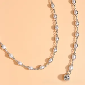 Détail d'une ceinture chaîne en perles avec billes en métal argenté et breloque polie