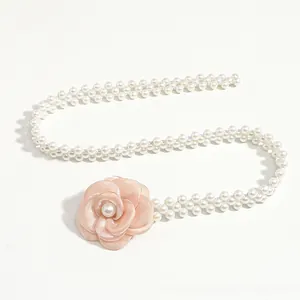 Detailed macro view of white faux pearl waist chain with a soft pink fabric camellia flower