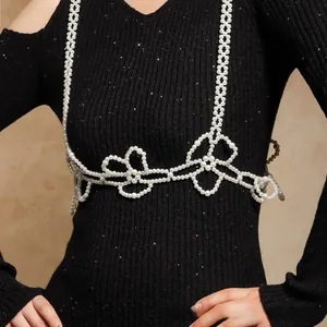 Detailed view of pearl body chain with floral bow design over black knit top