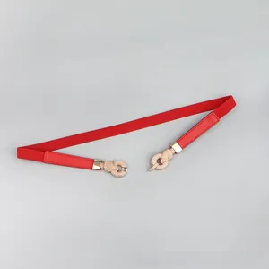 Detail of red elastic skinny belt with a gold intertwined buckle on grey background
