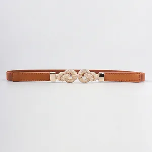 Detail of a thin elastic brown waist belt featuring a gold interlocking knot metal buckle