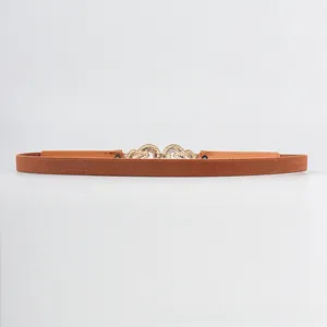 Detail of caramel elastic waist belt featuring an ornate gold filigree metal buckle