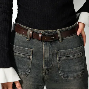Detail of a dark brown slim leather belt with vintage metal buckle on teal jeans
