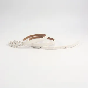 Détail de ceinture fine en simili cuir avec trois fleurs blanches et boucles dorées