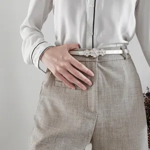 Détail d'une fine ceinture blanche avec trois boucles de fleurs dorées sur un pantalon gris