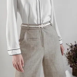 Détail d'une ceinture fine blanche avec boucle fleurie dorée sur un pantalon gris