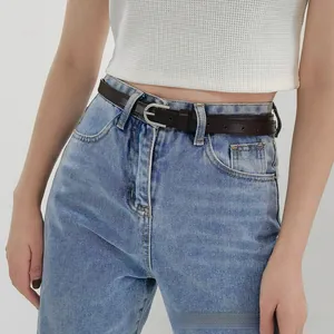Gros plan d'une fine ceinture en cuir marron foncé avec boucle en D argentée sur un jean