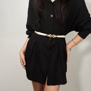 Detail of a beige elastic skinny belt with a gold knot buckle on a black shirt dress