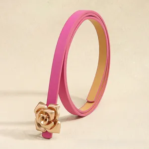 Close-up of a slim pink leather belt with a 3D golden rose metal buckle on beige background