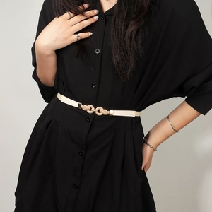 Close-up of a cream elastic waist belt with a gold interlocking ring buckle on a dress