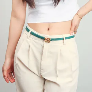 Detail of slim dark green belt with gold rose buckle on beige pants for women