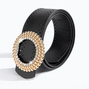 Détail d'une ceinture en cuir noir à œillets et boucle ronde dorée avec strass brillants
