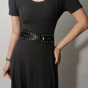 Détail d'une large ceinture punk noire à rivets argentés sur une robe grise