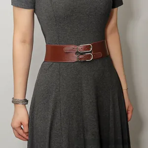 Détail d'une large ceinture élastique marron à double boucle portée sur une robe grise