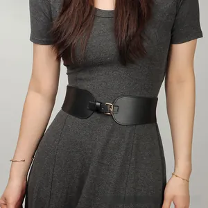 Détail d'une large ceinture élastique noire avec boucle dorée sur robe grise